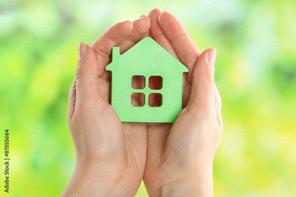 Female hands holding model of house on bright background
