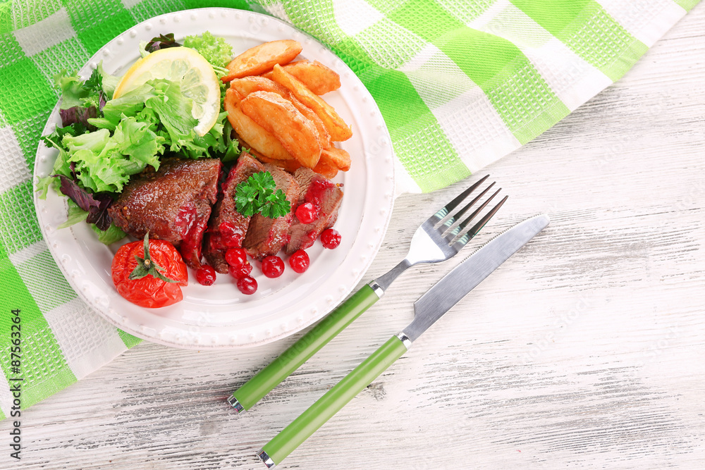 Tasty roasted meat with cranberry sauce and roasted vegetables on plate, on color wooden background Tasty roasted meat with cranberry sauce and roasted vegetables on plate, on color wooden background