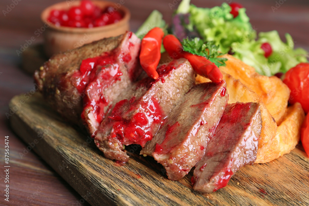 Beef with cranberry sauce, roasted potato slices on cutting board, on wooden background Beef with cranberry sauce, roasted potato slices on cutting board, on wooden background