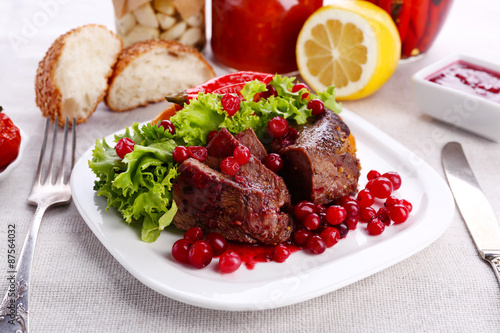 Tasty roasted meat with cranberry sauce on plate, on light background