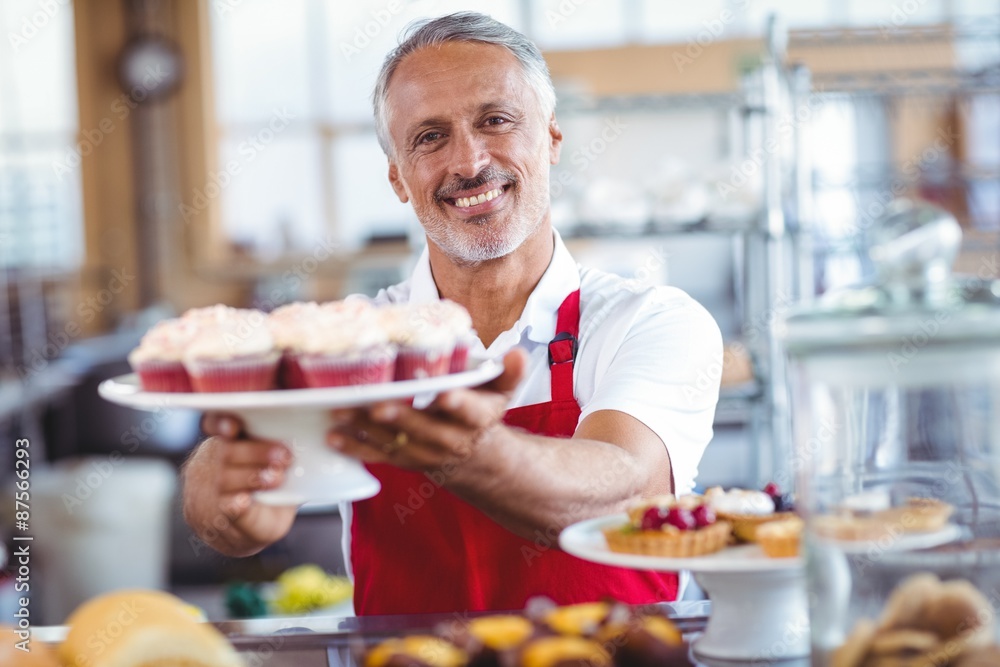 Happy barista smiling at camera and holding a plate of cupcakes