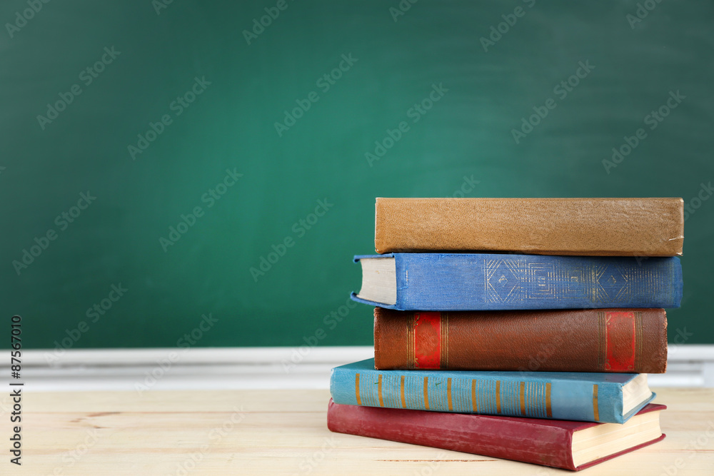 Stack of books on desk, on blackboard background Stack of books on desk, on blackboard background
