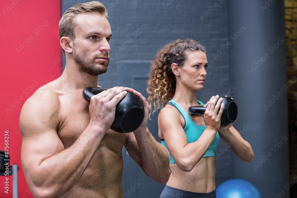 Muscular couple exercising with kettlebells