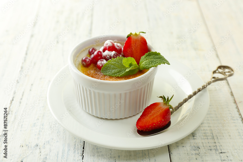 Creme brulee dessert with fresh strawberries and mint leaves, on color wooden background Creme brulee dessert with fresh strawberries and mint leaves, on color wooden background