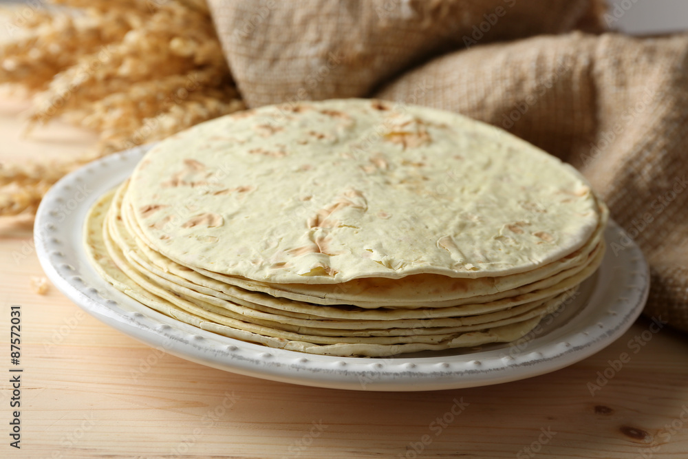 Stack of homemade whole wheat flour tortilla on plate, on wooden table background Stack of homemade whole wheat flour tortilla on plate, on wooden table background