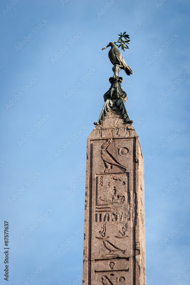 Egyptian Obelisk. Close detail of the top of an Egyptian obelisk featuring hieroglyphs and a bronze cast of a dove holding an olive branch in its beak.