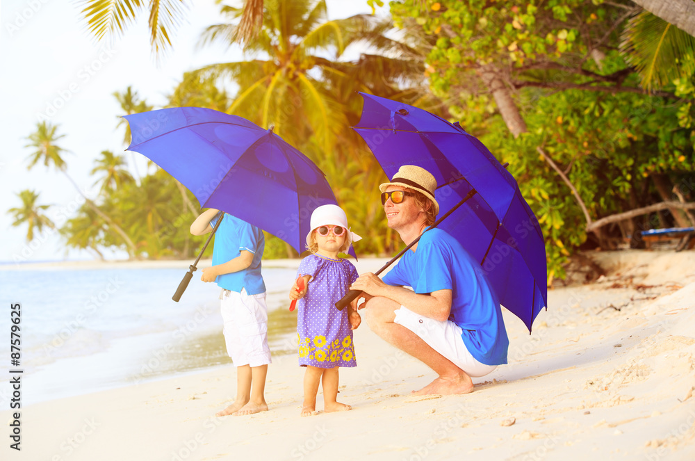 Father and kids at beach with umbrellas to hide from sun