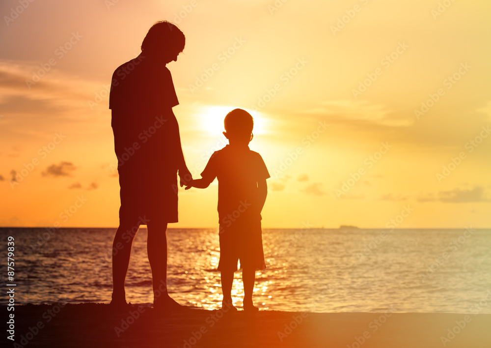 silhouettes of father and son holding hands at sunset