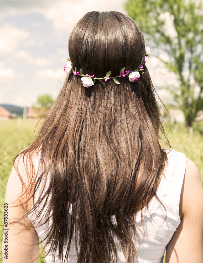 Naklejka premium Beautiful long woman's hair with the flower in the head, standing in the meadow