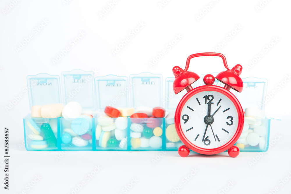 Medicine in weekly pill box and red alarm clock Medicine in weekly pill box and red alarm clock