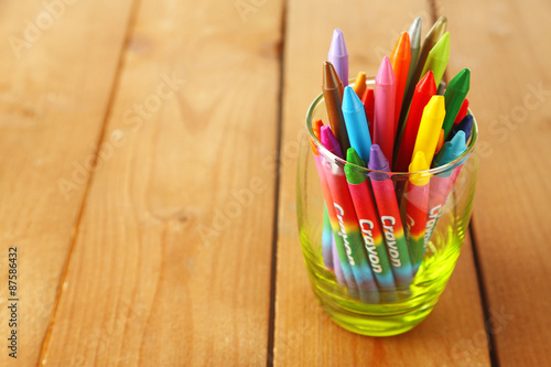 Colorful pastel crayons in glass on wooden background