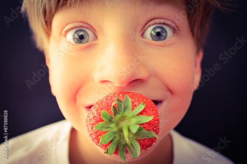 Wide eyed child with a fresh strawberry in his mouth
