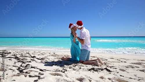 Couple in Santa Claus hats kissing on tropical beach with turquoise sea water
