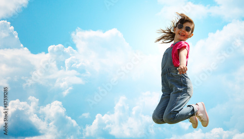 happy little girl jumping high over blue sky