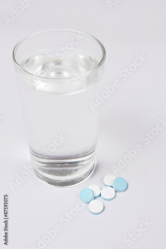 A glass of water and Pills, medicals, drugs, tablets in white