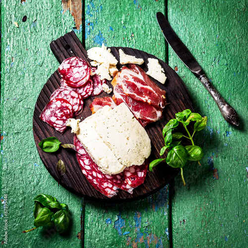 Meat and cheese on dark chopping board.