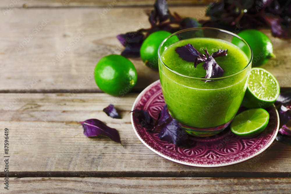 Glass of green healthy juice with basil and limes on table close up Glass of green healthy juice with basil and limes on table close up