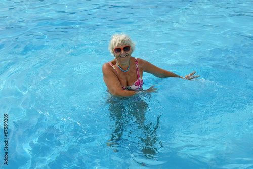 Aged woman is standing in bright blue pool water.