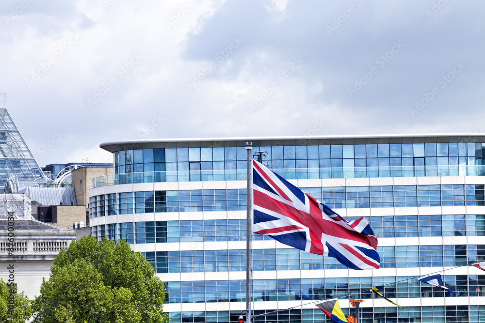 Waving in the wind British union flag in front of a glass window modern office building in London