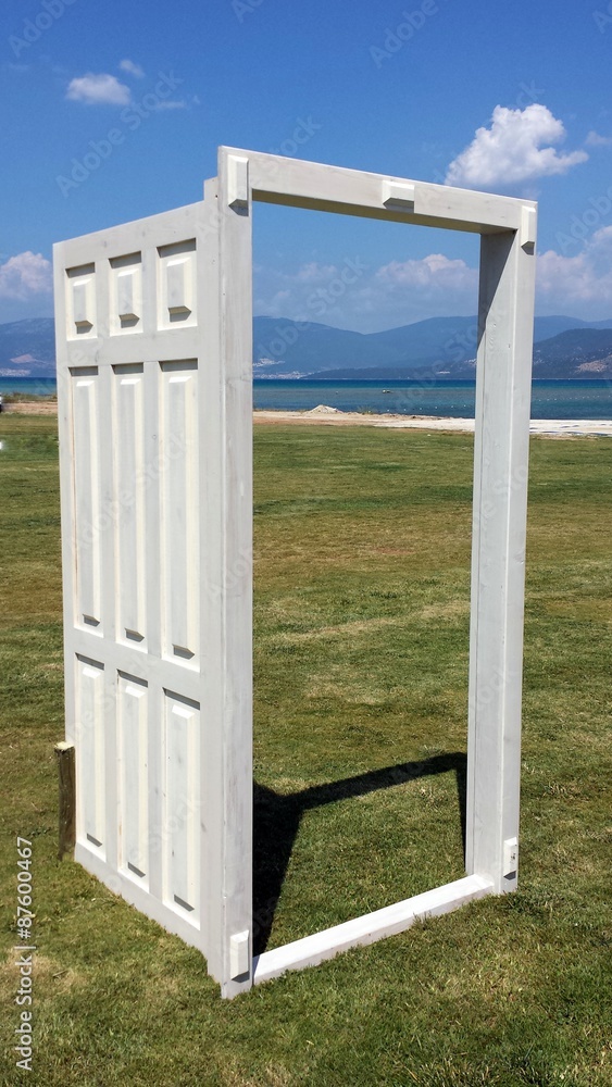 Fototapeta premium White open door on the grass overlooking the sea