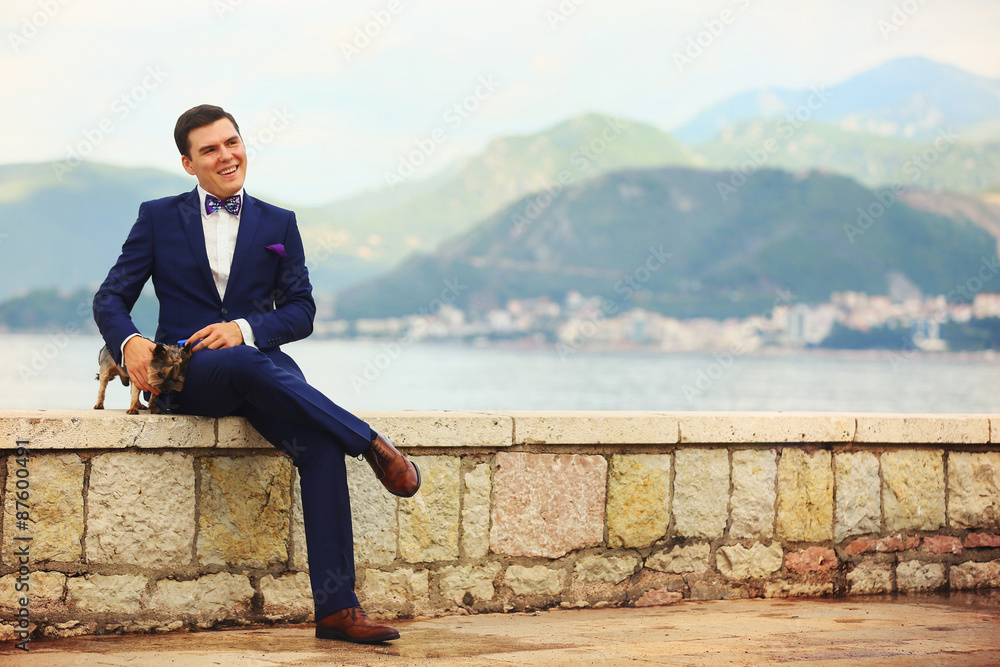 happy smiling stylish rich groom sitting on a pier holding a Yor