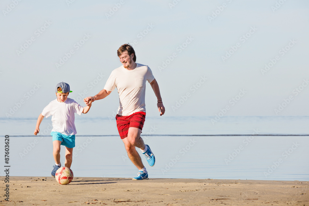 Happy father and son play soccer or football on the beach