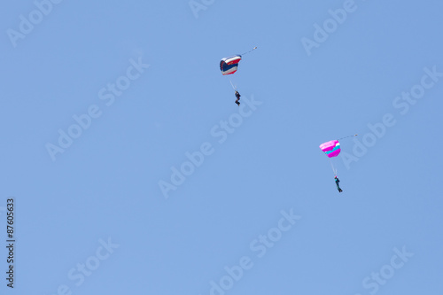 Parachutist on a blue parachute and parachutist on a pink parachute on background clean blue sky 