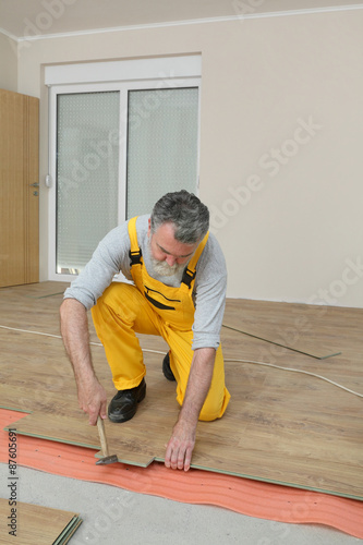 Laminate flooring of room, worker placing plank, using hammer