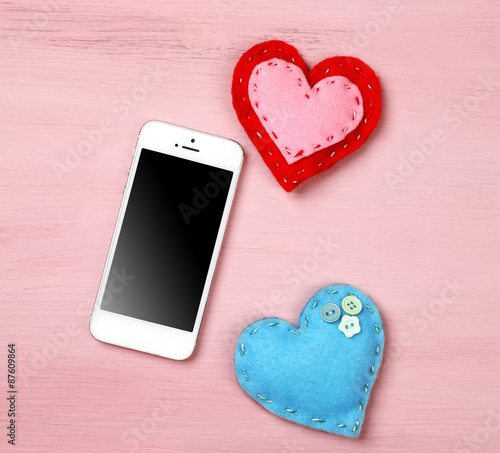 White smart phone with hearts on wooden desk.