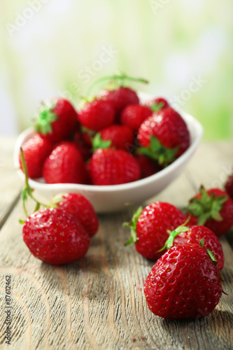 Ripe strawberries in saucer on wooden table on blurred background