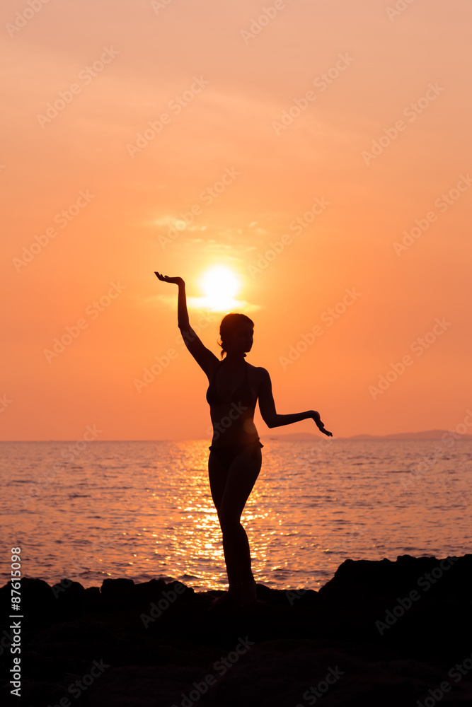 Standing woman silhouette in yoga pose on sunset sea background back lit