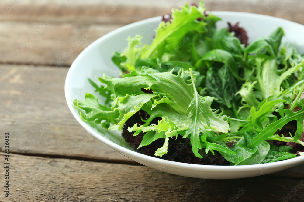 Bowl of mixed green salad on wooden table, closeup Bowl of mixed green salad on wooden table, closeup