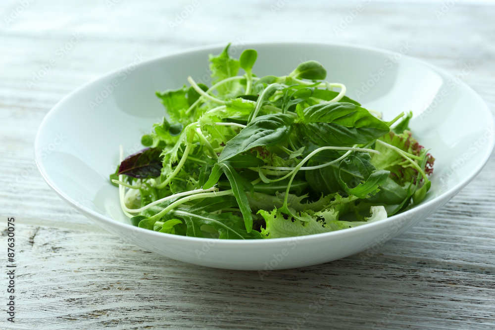Fresh mixed green salad in bowl on wooden table close up Fresh mixed green salad in bowl on wooden table close up