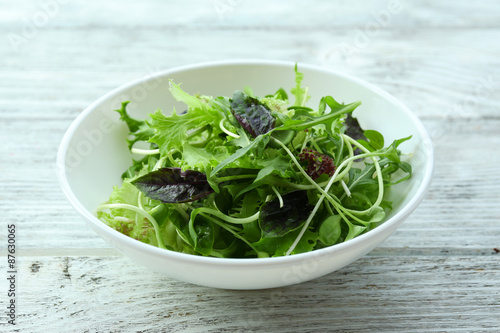 Fresh mixed green salad in bowl on wooden table close up