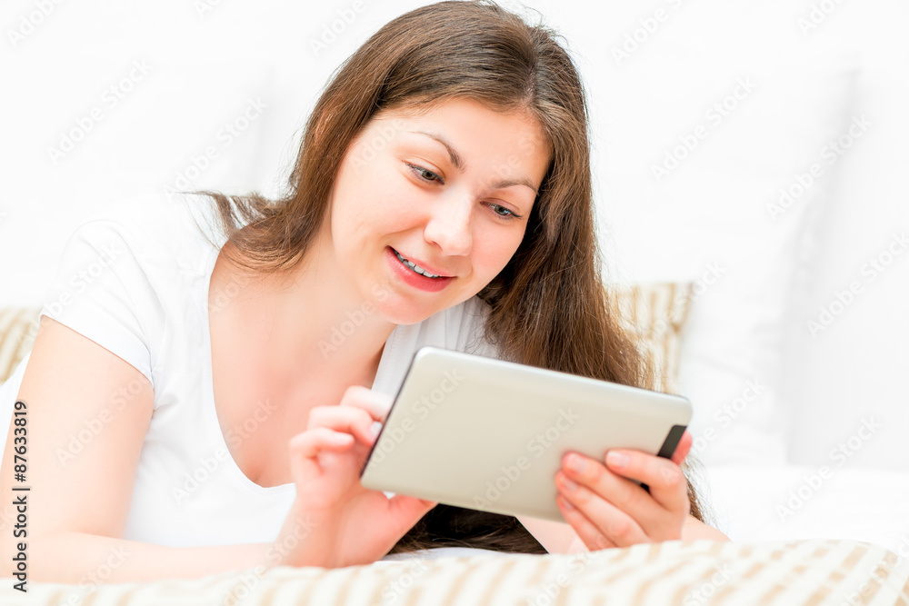 woman with tablet resting on a bed in a bedroom woman with tablet resting on a bed in a bedroom