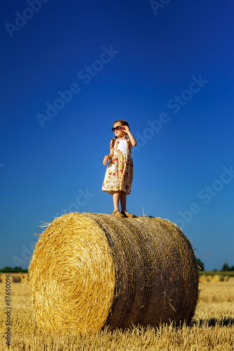 Cute little girl with sunglasses posing on the haystack