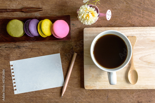 colorful macaroons with coffee and blank note on wooden table