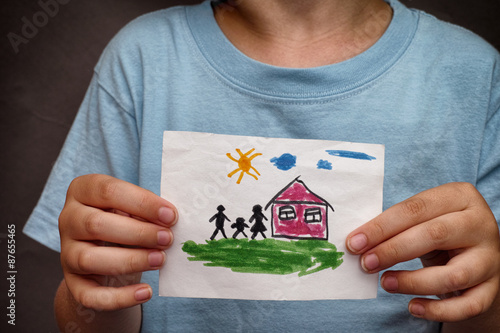 Child holds a drawn house with family photo