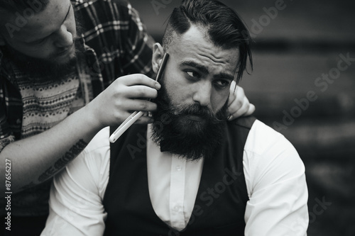 Fotografering barber shaves a bearded man