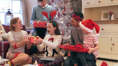 Family at christmas time trying to guess what their presents are before they open them. They are sitting together on the floor near the christmas tree in their home.