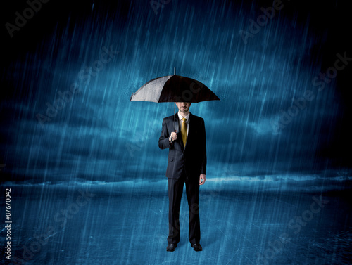 Business man standing in rain with an umbrella