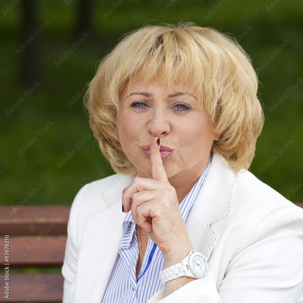 Portrait of old blonde woman with finger on lips