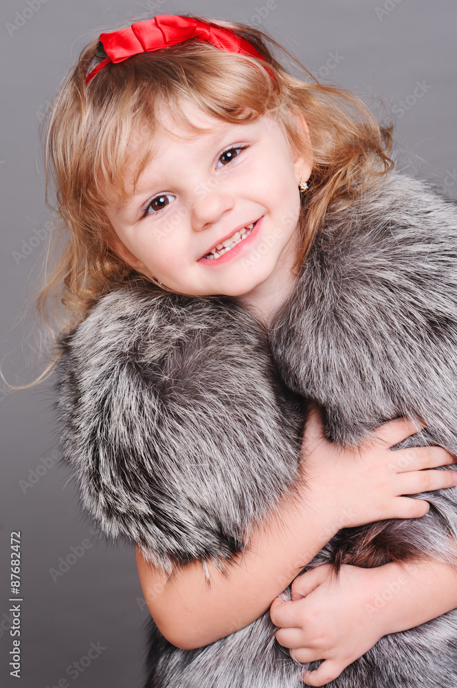 Smiling baby girl wearing fur clothes over gray. Looking at camera. Childhood. 