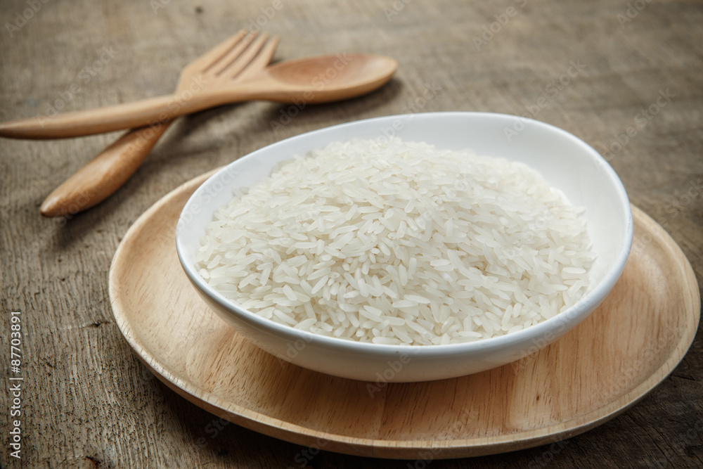 White rice grains with wooden spoon on wooden table - soft focus