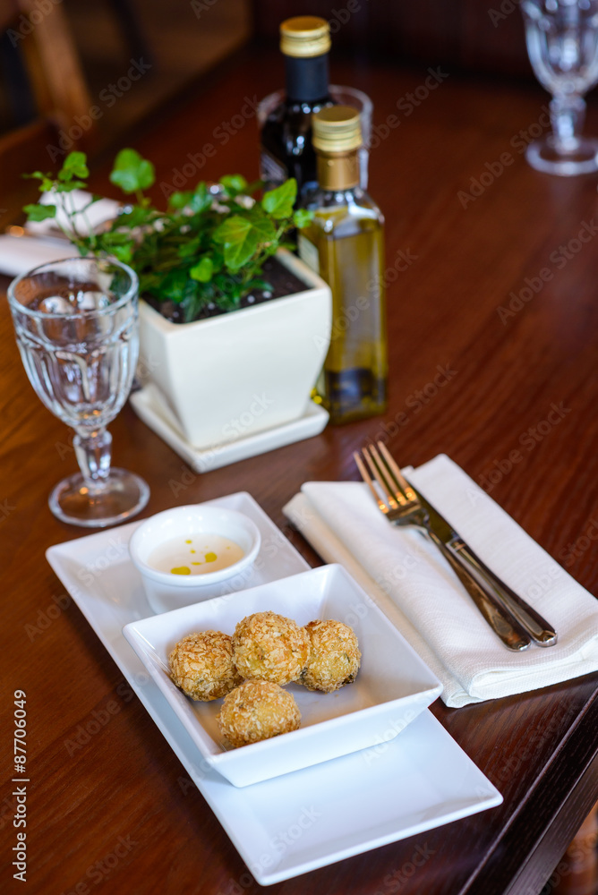 Fried potato balls with sauce on served restaurant table/Dish of fried potato balls on wooden table with cutlery,napkin and empty wine glass