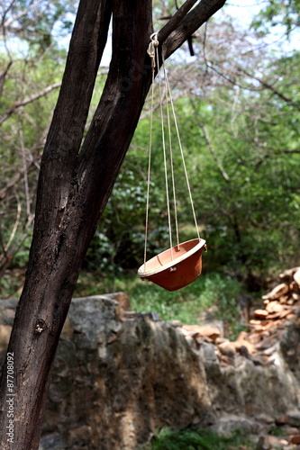 small semi flat pot made of clay being hung by ropes on tree for birds to drink water in hot summers 