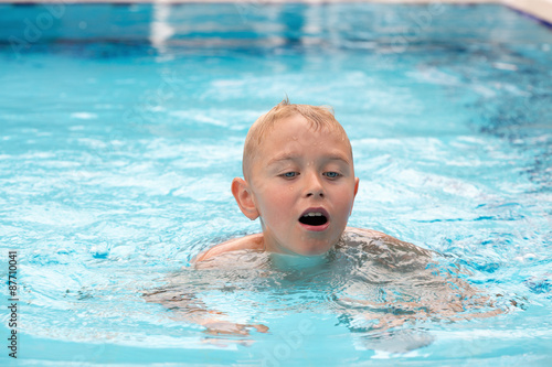 A cute blonde boy swimming in a swimming pool
