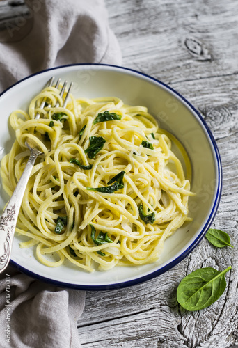 pasta with spinach and cream sauce on vintage enameled plate on a light wooden background