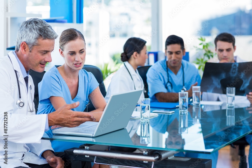 Doctor and nurse looking at laptop with colleagues behind