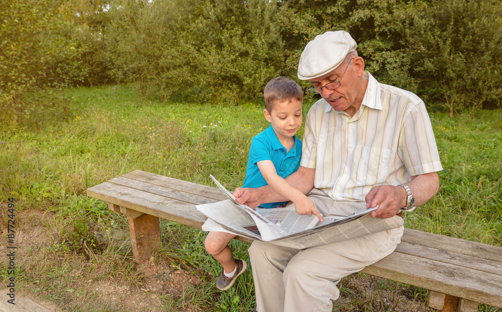 Senior man and child reading a newspaper outdoors Senior man and child reading a newspaper outdoors